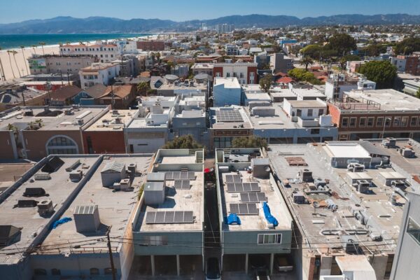 Drone view of a coastal urban area with rooftops and solar panels under a clear blue sky.