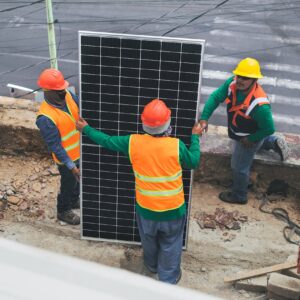 Workers wearing PPE install solar panels for sustainable energy at a construction site.