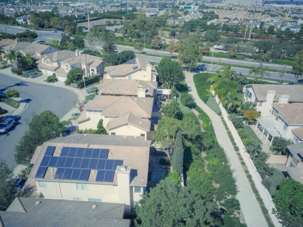 Aerial shot of suburban homes featuring solar panels and green landscapes.